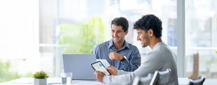 Two men reviewing business data on a tablet, potentially discussing how to get start your business in Dubai.