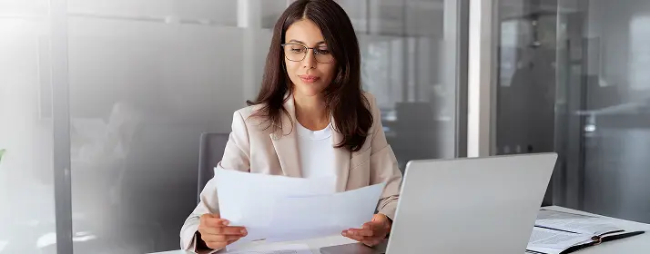 Businesswoman reviewing documents at her desk with a laptop, starting a business in Dubai.