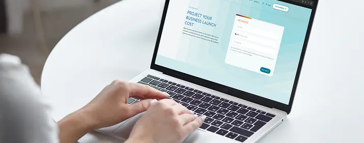 Person using laptop to project business launch cost in Dubai, with "Get Started" form visible.